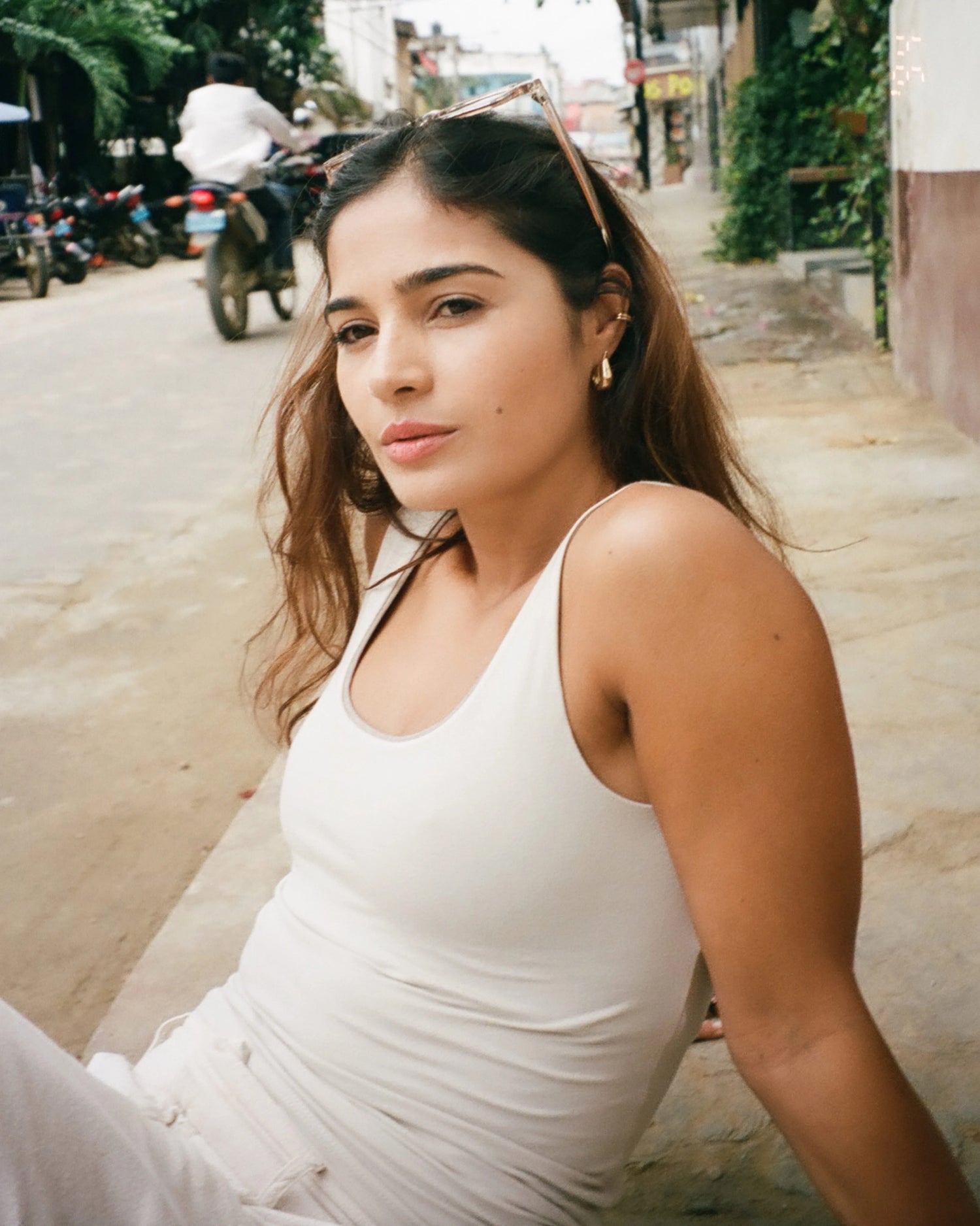 Model wearing birch close-to-body cropped tank with wide straps and built-in shelf bra, seated on a street