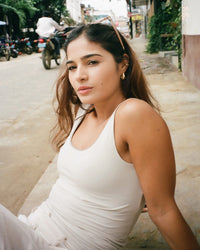 Model wearing birch close-to-body cropped tank with wide straps and built-in shelf bra, seated on a street