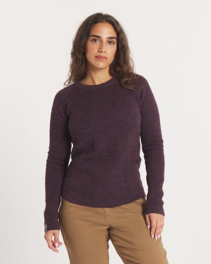 Woman wearing the PAKA Women's Mountain Crew in Eggplant and beige pants on a white background