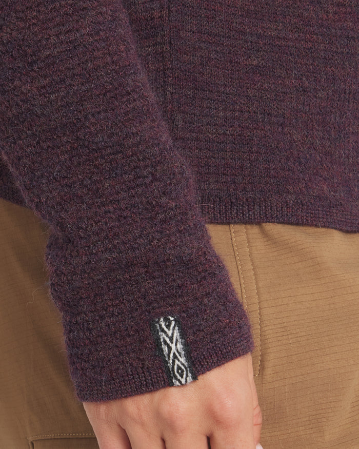 Close-up of Women's Mountain Crew in Eggplant sweater sleeve with a brand logo on a brown background