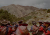 Group of Peruvian women in embroidered hats and shawls sitting on a hillside with terraced Andean mountains behind them