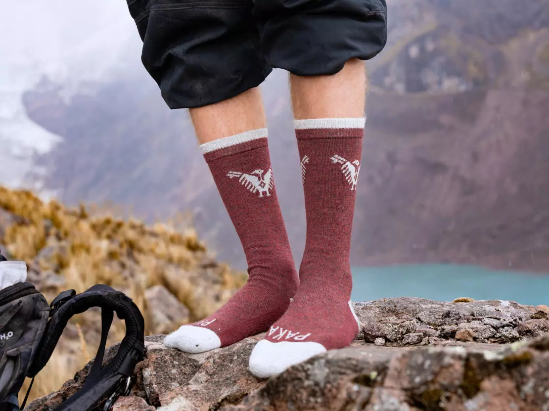 Someone wearing our Condor socks over a rock in front of a mineral blue lake