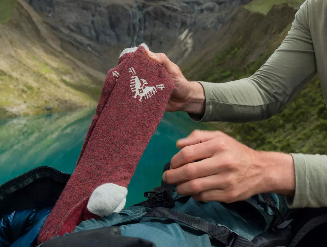 Someone holding up our condor socks in front of a mineral blue lake 