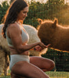 A women wearing alpaca underwear feeding a brown alpaca under the sunshine 