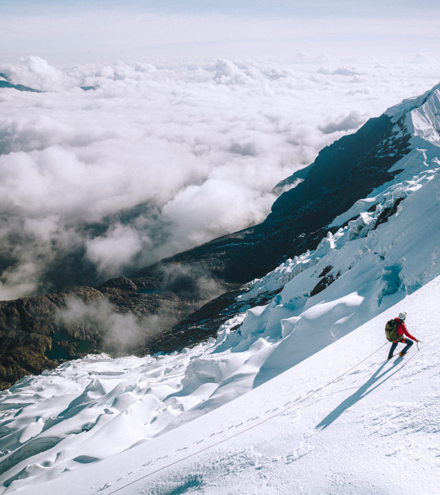 A man climbing a snowy mountain waring our red Pakafill Puffer jacket