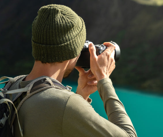 Man taking picture with camera in front of blue lake 