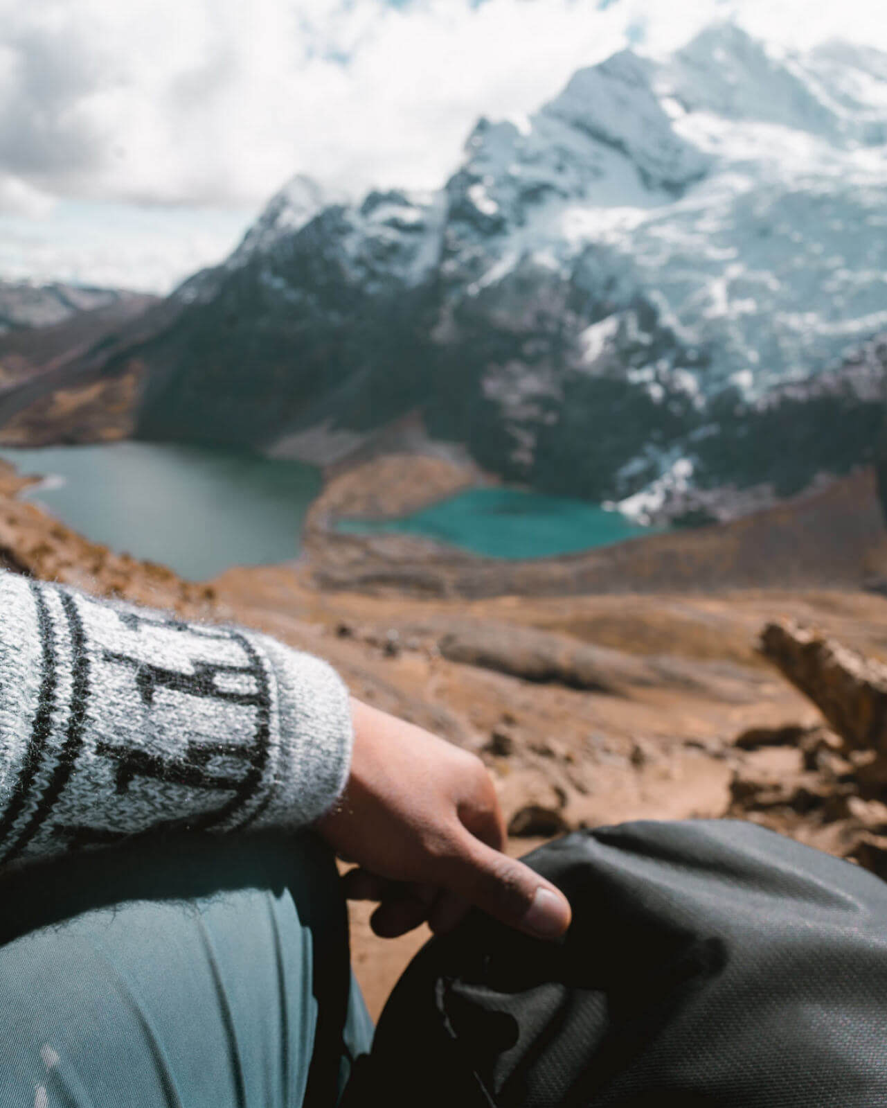 Person wearing alpaca sweater in Peru looking over lakes at the base of a mountain 