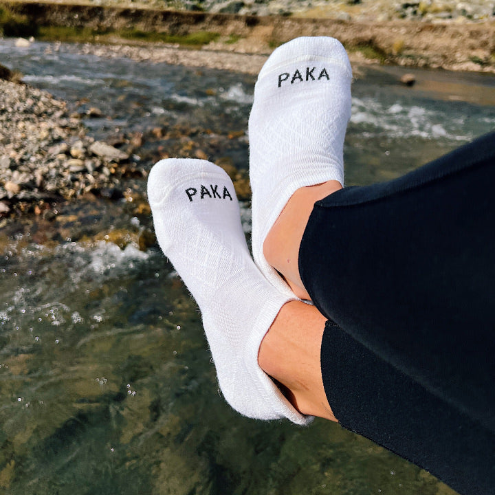 A pair of cozy white alpaca Ankle socks in front of a river