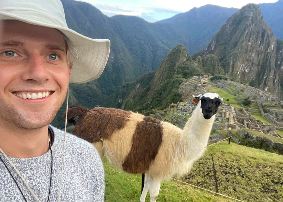 Zael smiling in Machu Picchu with an alpaca behind him