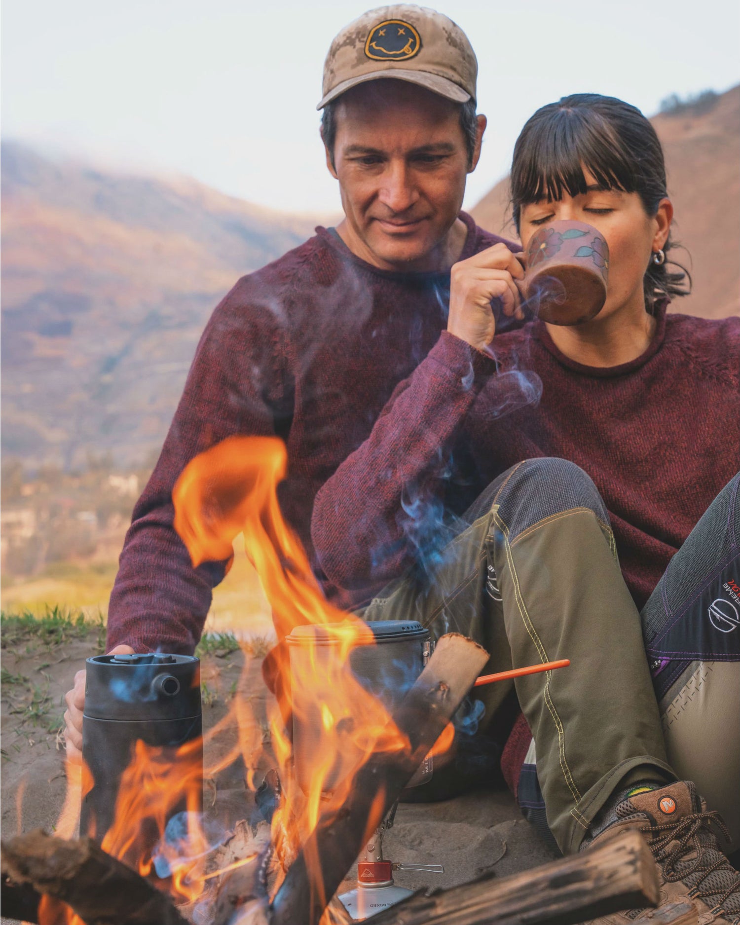 Man and woman by bonfire wearing two red cusco alpaca sweater with alpaca design on side