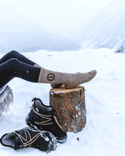 Timber / Tan Cozy Natural Fiber Alpaca Wool Crew Socks on Feet Resting on Stump in Snowy Mountains – PAKA Apparel