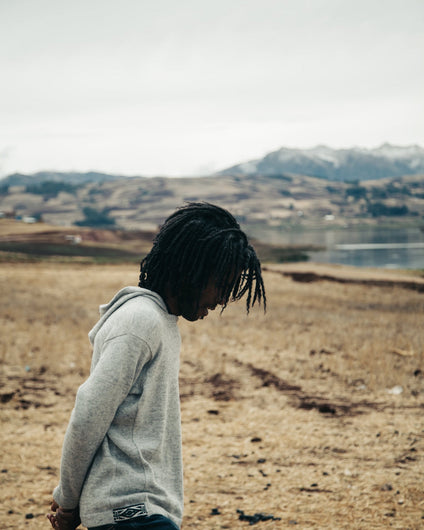 Man Wearing The Hoodie Light Grey Alpaca Wool Hooded Knit Sweater in Front of Lake and Mountains in Chinchero, Peru – PAKA Apparel
