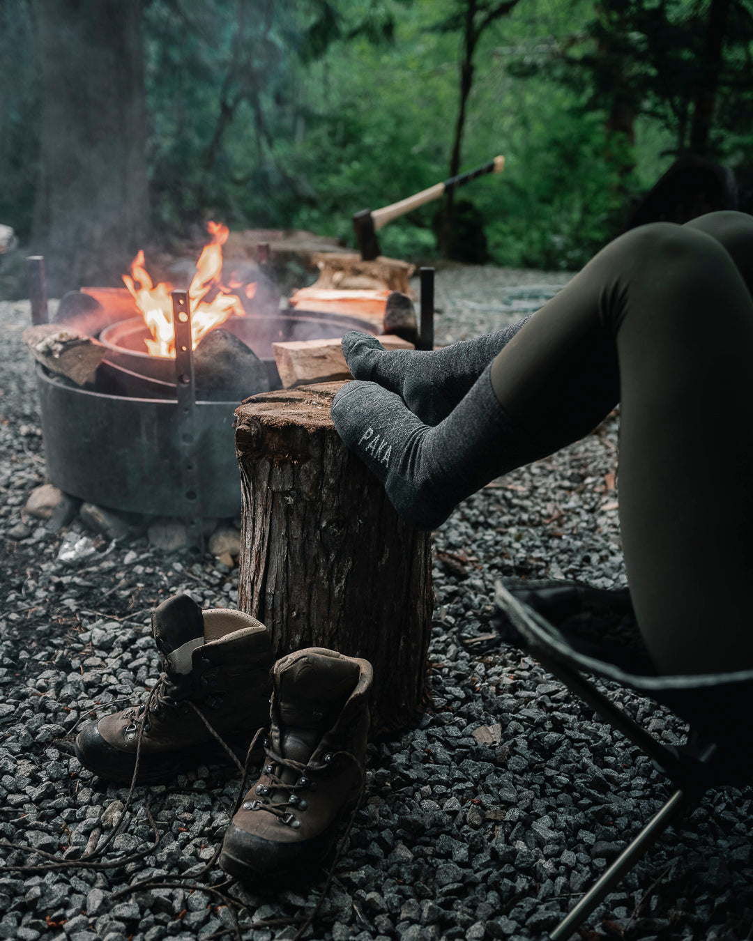 Dark grey Paka socks on wooden stump in front of boots and campfire