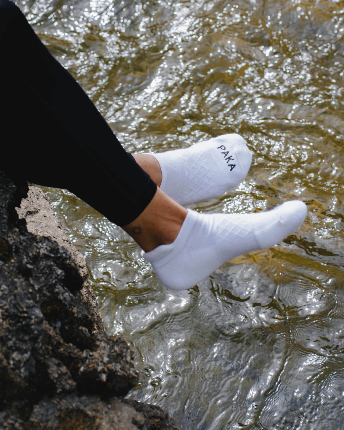 Woman dangling feet over river wearing white alpaca wool ankle socks 